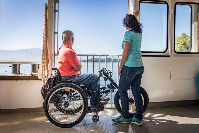 Mann im Rollstuhl und Frau genießen Ausblick vom Schiff auf den Chiemsee