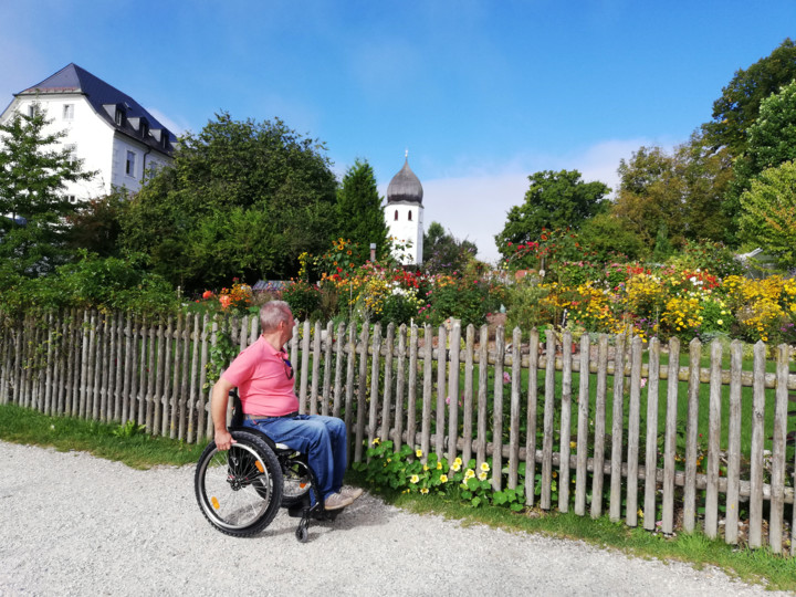 Mann im Rollstuhl seht vor dem Klostergarten auf der Fraueinsel und begutachtet die bunten Blumen